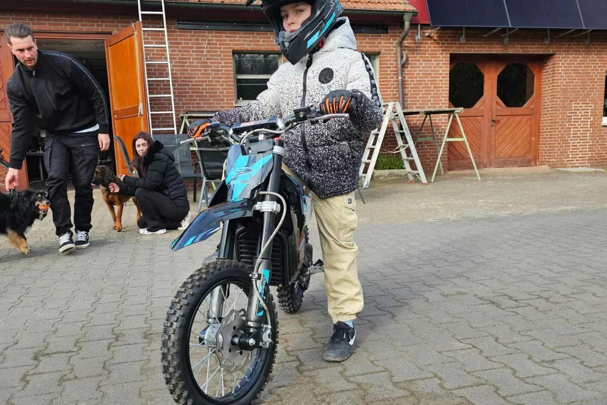 Kind op een blauwe elektrische dirtbike op de oprit