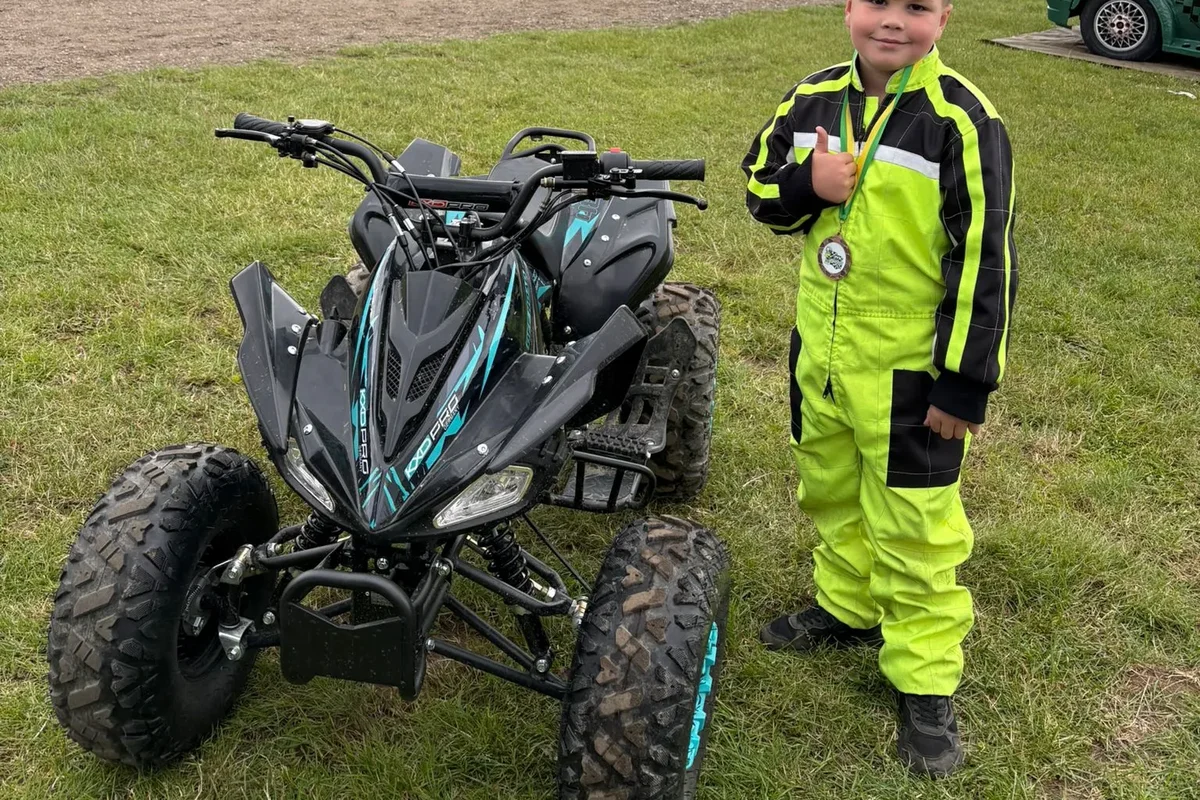 Jongen in geel racepak naast zijn quad