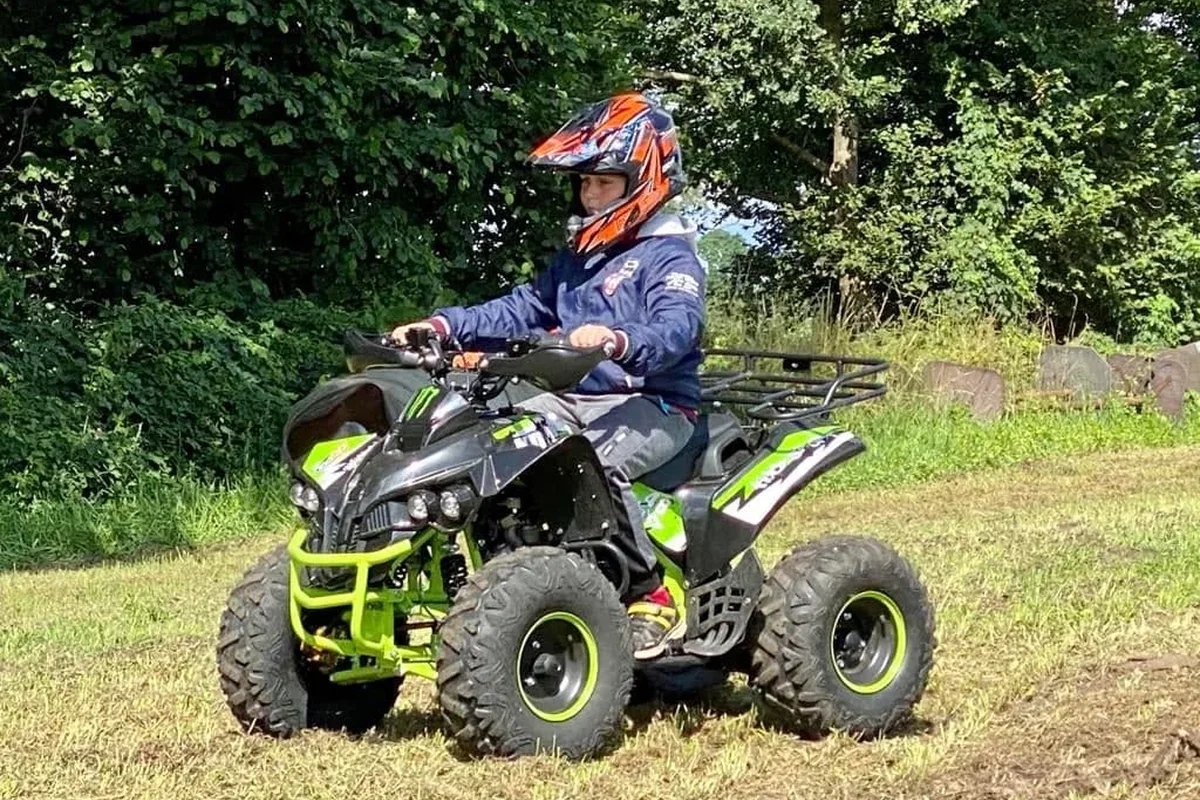 Kind in oranje helm op een groene quad in het veld