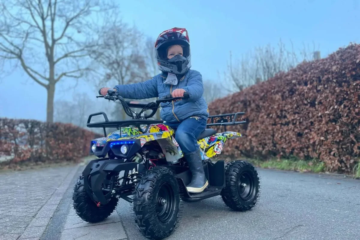 Kind op een kleurrijke kinderquad bij een haag